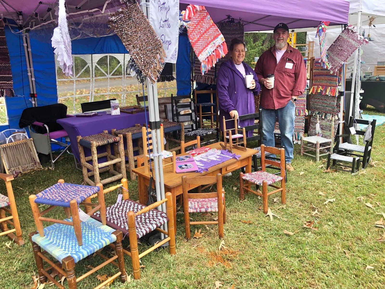 Patty's Little Shop booth under a purple tent, with twined rugs and rewoven chairs